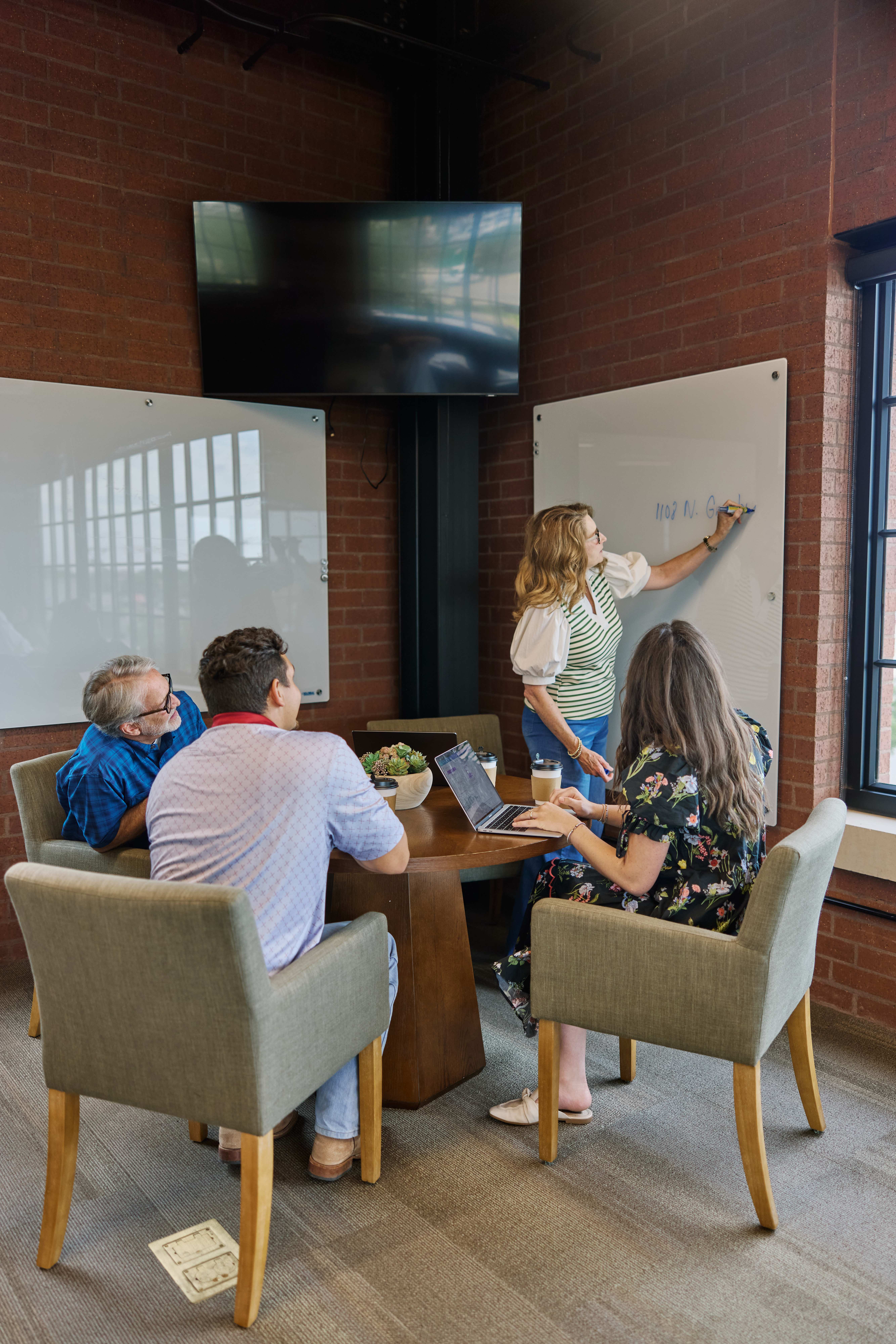 A member sketching ideas on a glass whiteboard while colleagues work nearby